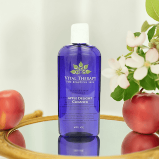 Vital Therapy Apple Delight Cleanser for skincare, soy-free and non-GMO, displayed with apples on a mirror.