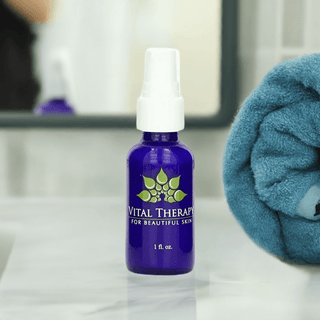 Blue bottle of Vital Therapy skin lightening lotion on a bathroom counter with a towel in the background.