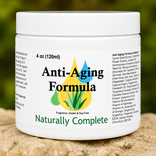 A white plastic jar of 'Anti-Aging Formula' with a white lid, set on a textured stone surface with a blurred green garden background. The label features a colorful graphic of a yellow, green, and blue droplet shape above the text 'Anti-Aging Formula' and 'Naturally Complete'.